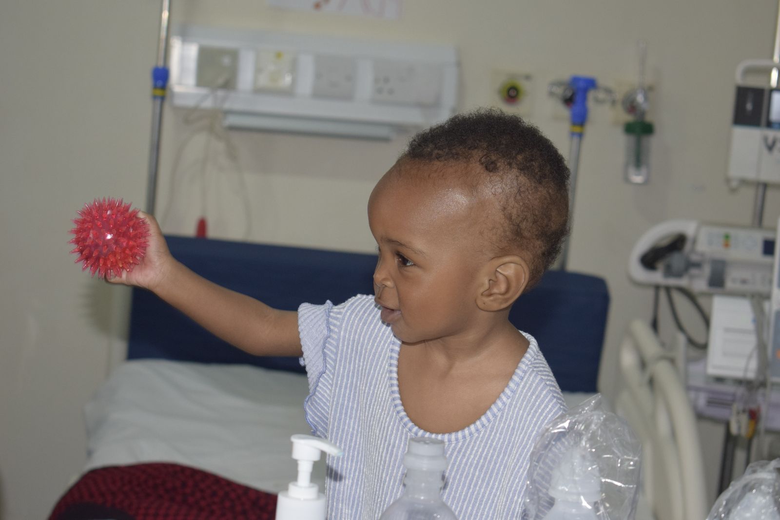 A child on a hospital bed holds up a red spiky ball after treatment
