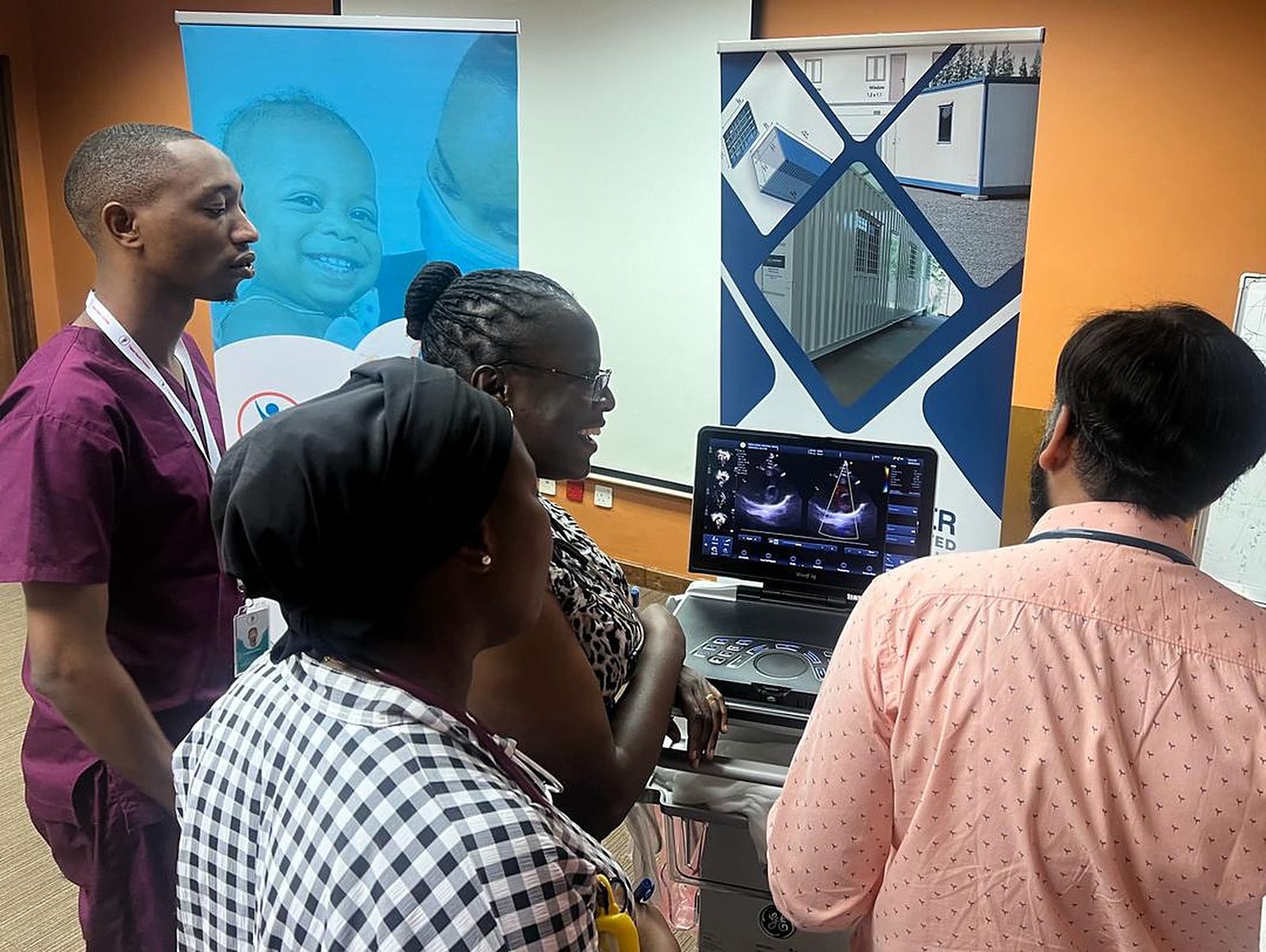 Clinicians and a family at an echo screening station in front of One New Heart banners