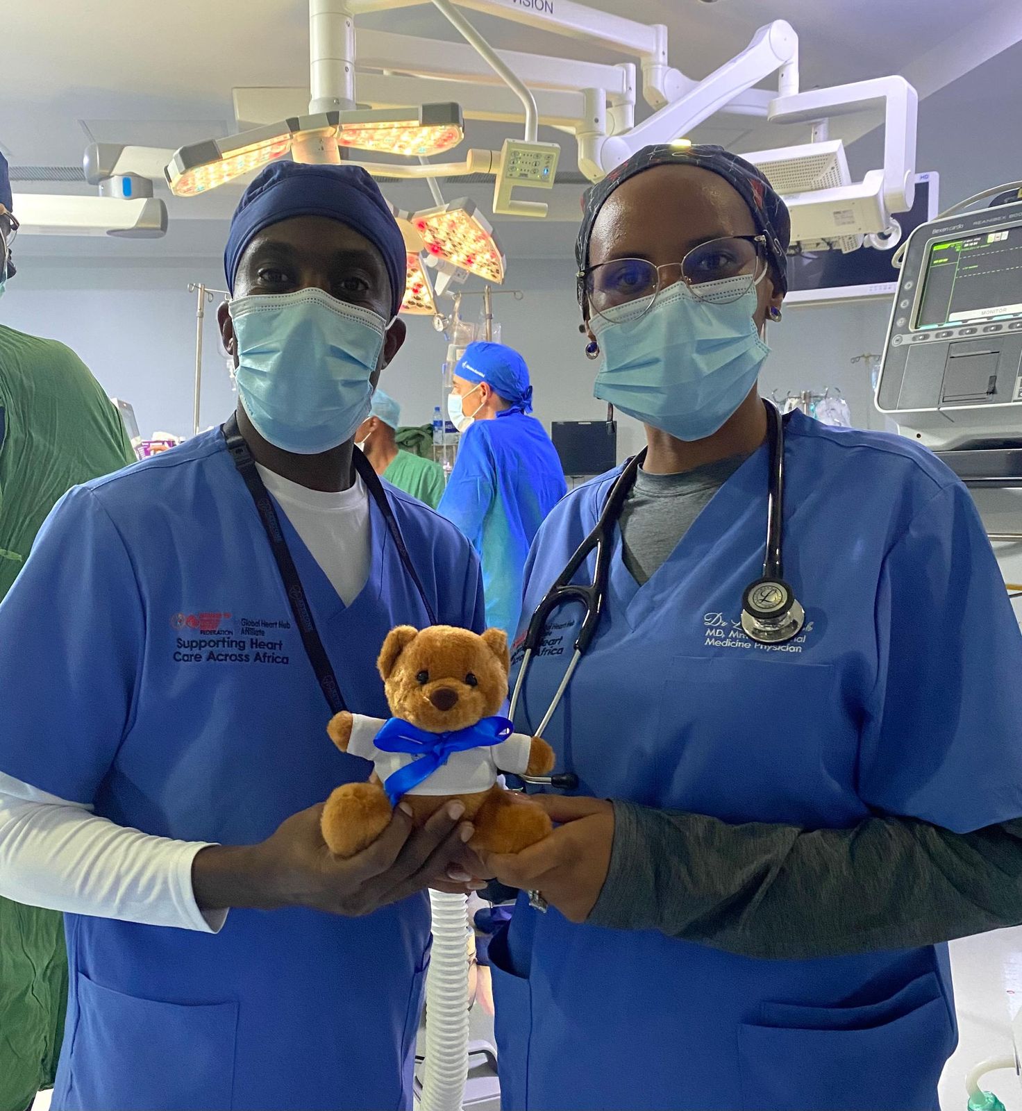 Two theatre staff in scrubs, one holding a teddy bear, during a surgical camp